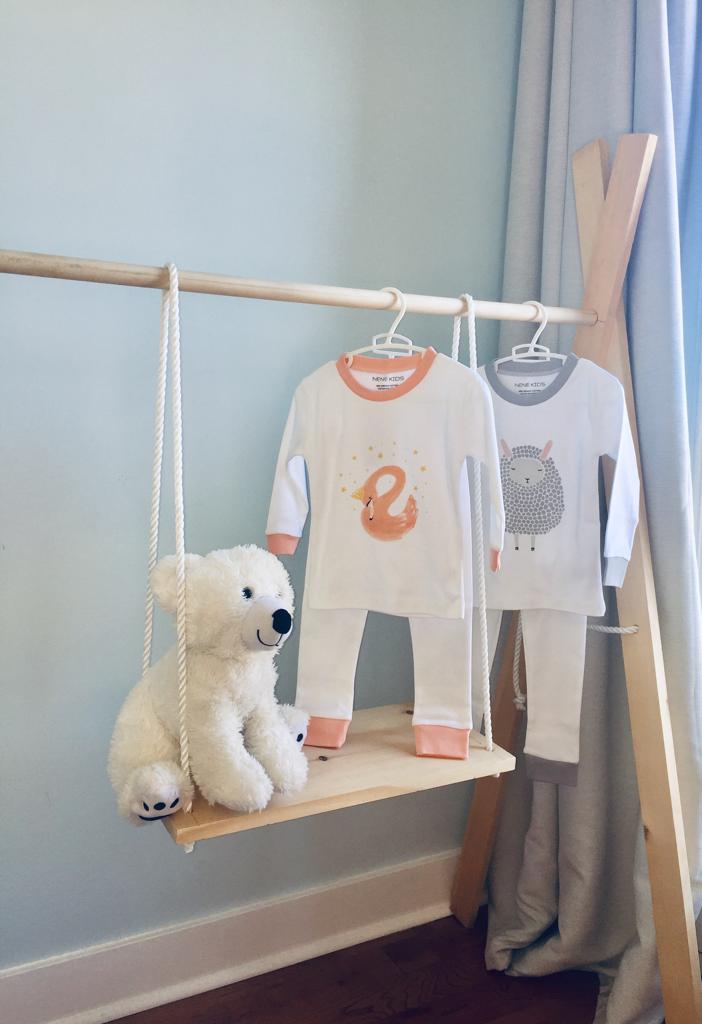 Noah & She Sleepy Lamb and Elegant Swan pajama sets hanging on a wooden rack in a nursery